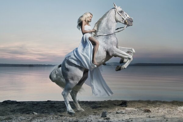 Una chica con un vestido blanco se sienta en un caballo blanco. Lago de fondo