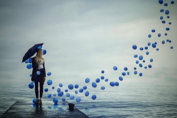 Ein Mädchen mit einem Regenschirm schaut hinter den fliegenden Luftballons in den Himmel