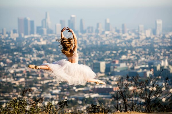 A girl in a white dress dances against the background of the city