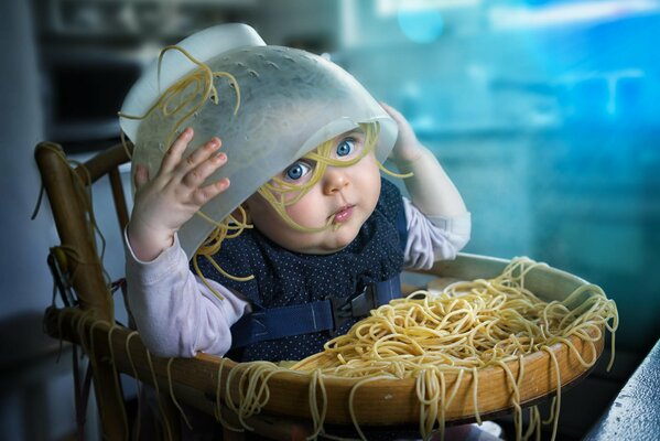 Bambino piccolo con un piatto di spaghetti in testa