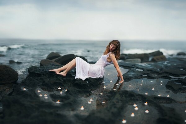 The girl is sitting on the rocks near the sea