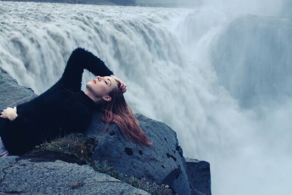 Ein Mädchen in Schwarz liegt am Rande eines Wasserfalls