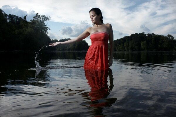 Das braunhaarige Mädchen in einem roten Sommerkleid kniet im Wasser