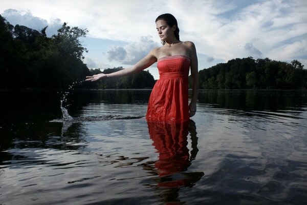 Chica de pelo oscuro en vestido rojo de pie hasta las rodillas en el agua