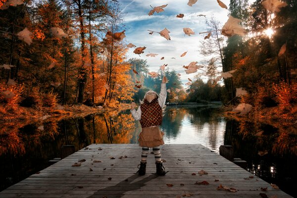 Mädchen auf der Brücke am Fluss spielt mit Herbstlaub