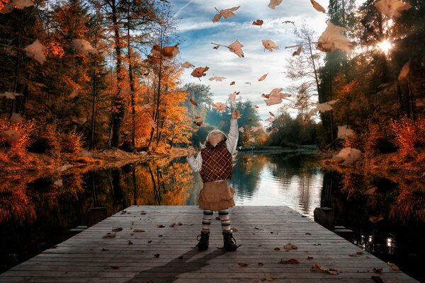 Dziewczyna na moście nad rzeką bawi się jesiennymi liśćmi
