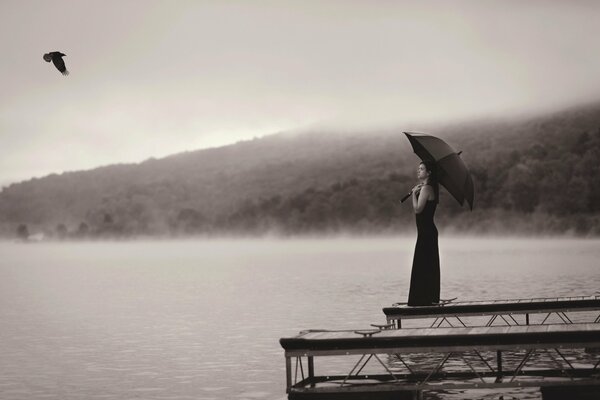 The girl is standing on the shore of the lake. A lonely bird is flying above her