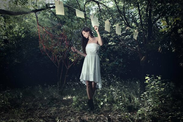 A girl in a white dress hooks sheets of a book on a rope with clothespins, everything happens in the forest