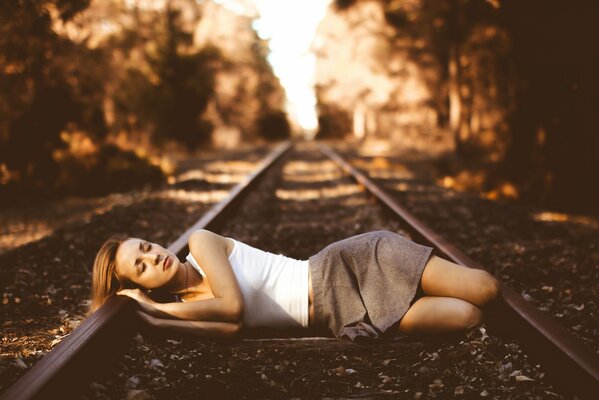 The girl is lying on the railway tracks