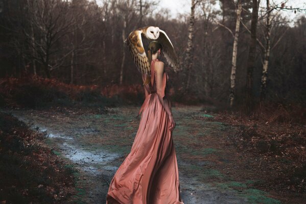 Mysteriöses Foto eines Mädchens in einem rosa Kleid im Wald mit einer Eule