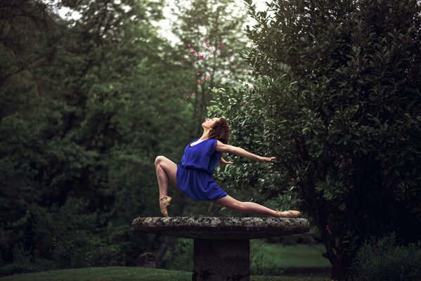 Девушка в синем платье делает упражнения в лесу