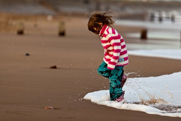 Fille sur la plage dans la mousse des vagues de la mer