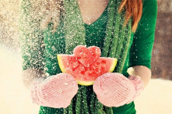 A red-haired girl in winter mittens holds a watermelon