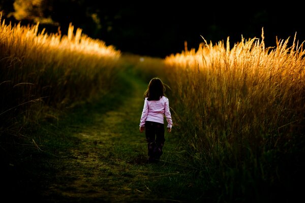 The girl from the back on the road among the tall ears