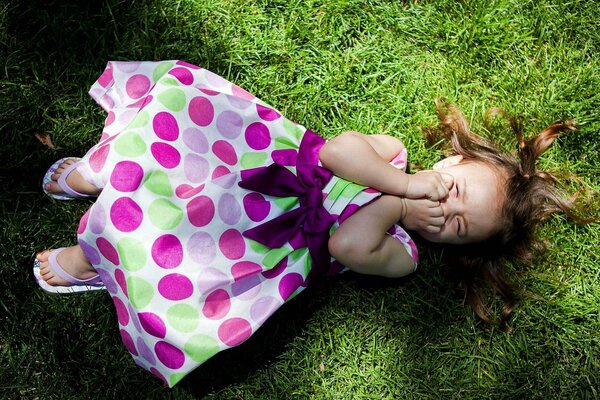 The girl is lying on the grass laughing in the rays of the sun