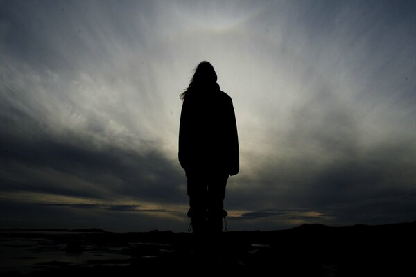 Figura humana oscura sobre un fondo gris con nubes