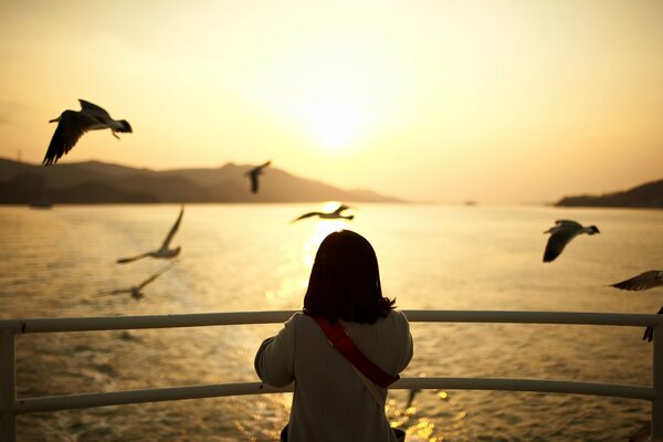 Una niña observa la puesta de sol en la popa de un barco