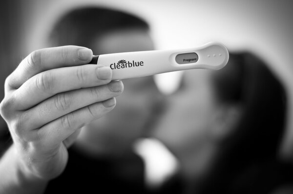 Happy people kissing in a black and white photo, holding a pregnancy test in their hand