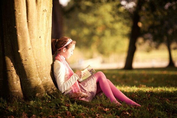 A girl is sitting under a tree and reading a book