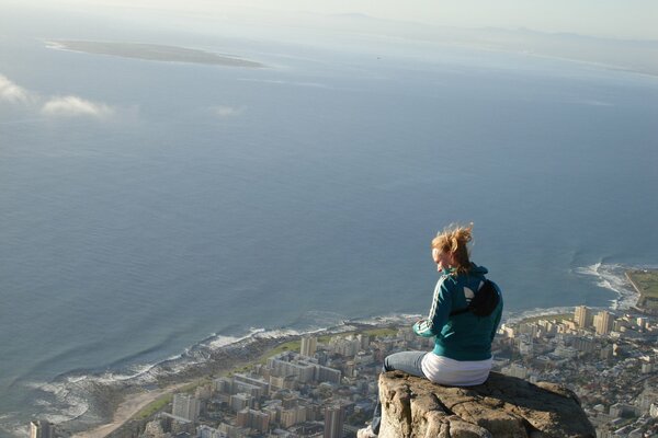 The girl is sitting on the edge of a high cliff