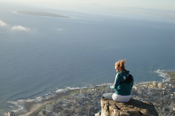 Девушка сидит на краю высокой скалы