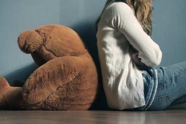 Fille assise dos à l ours en peluche