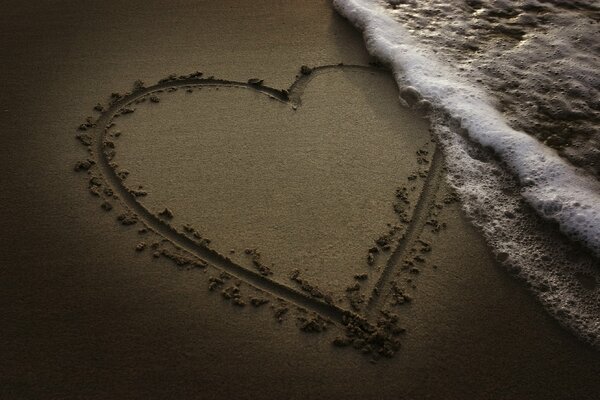 Gezeichnetes Herz auf dem Sand mit Wellen