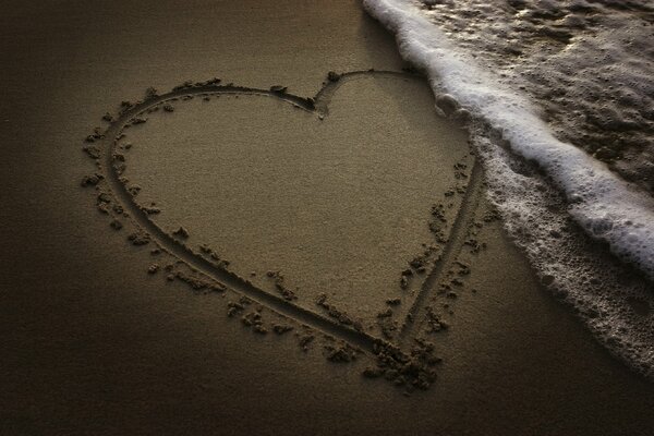 Coeur dessiné sur le sable avec des vagues