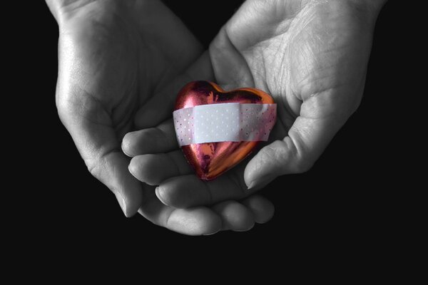 A woman holds a heart sealed with a plaster in her hands