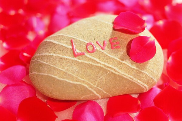 The inscription of love on a brown stone on a background of red petals