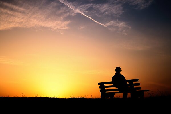 Homme sur un banc sur fond de coucher de soleil