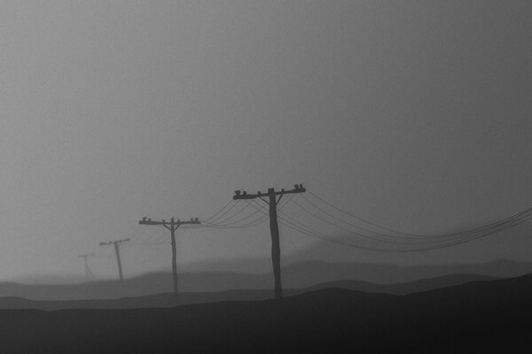 Poles with wires in the night fog. Greyness and gloom
