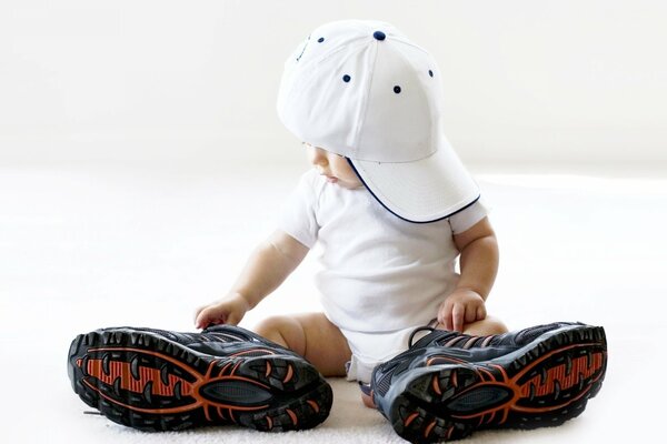 A little boy in big sneakers and a white cap