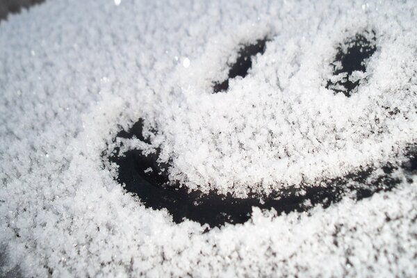 Ein gezeichneter Smiley auf einem schneebedeckten Glas