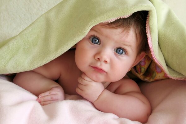 A small child peeks out from under the blanket