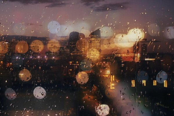 View of the rainy city at night with lights through the window