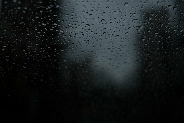 Gocce di pioggia su vetro su sfondo scuro
