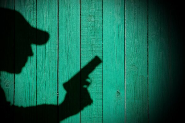 Shadow of a man with a gun on a green wooden background