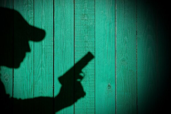 Ombra dell uomo con la pistola su sfondo di legno verde