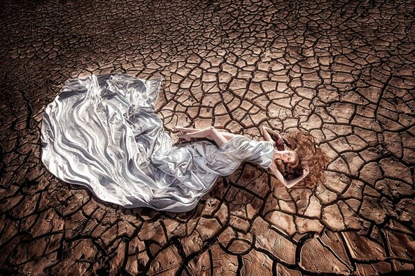 A girl in a chic dress on the background of the land of drought and cracks