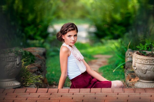 Niña en los escalones de ladrillos en el Jardín