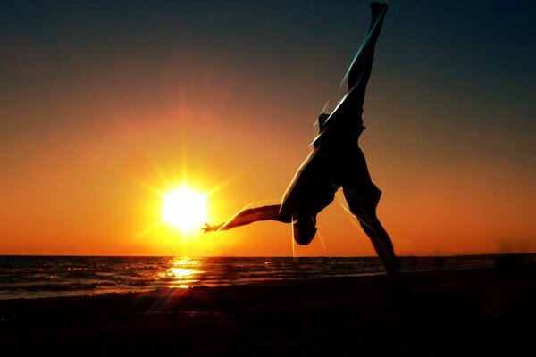 A man does gymnastics on the coast at sunset