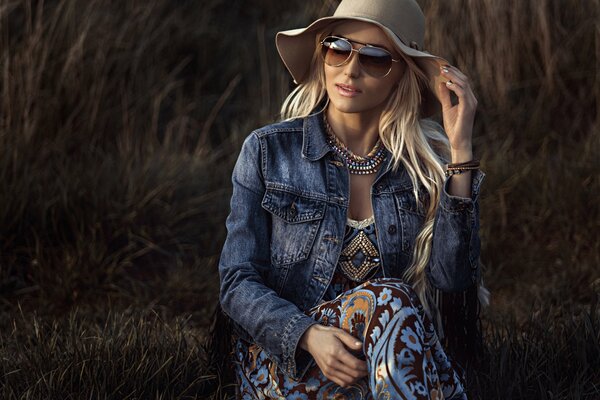 Blondine mit Hut und Brille auf dem Hintergrund eines Heuhaufens