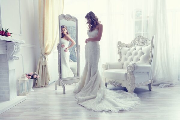 A bride in a wedding dress looks in the mirror