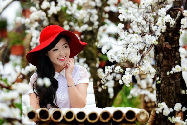 Asiatische Frau in einem Hut unter einem blühenden Baum