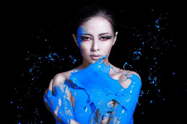 A girl in blue paint on a black background