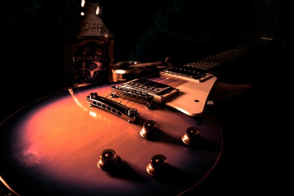 Электрическая гитара в темноте и бутылка виски