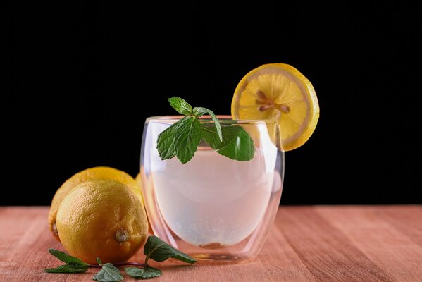 Sur la table se trouve un verre avec de la glace, une tranche de citron et de menthe, à côté se trouvent des Citrons et des brins de menthe