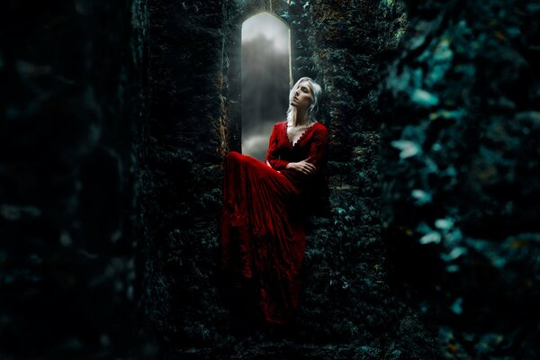 La chica del vestido rojo se sienta en un castillo sombrío