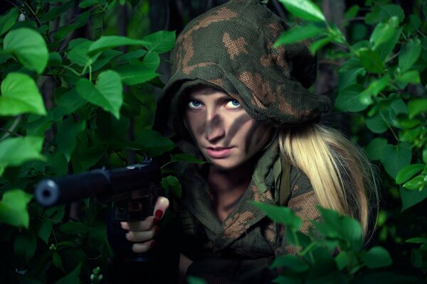 Una chica con ropa de camuflaje y pintura de combate de detrás de los arbustos apunta con una pistola